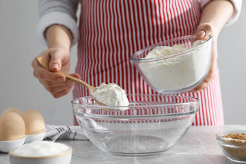 Making cinnamon rolls. Woman adding flour into bowl at gray marble table, closeup