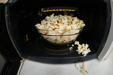 Bowl of tasty popcorn in microwave oven on white marble table, closeup. Fisheye lens effect