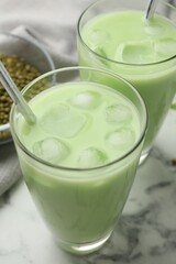 Fresh mung bean juice in glasses and seeds on white marble table, closeup