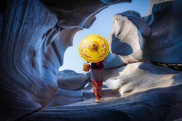  Asian tourist stands on a rock with a pattern created by water erosion over a long period of time.