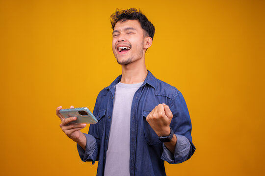 Excited Asian Man Gamer Playing Video Game On Mobile Phone Celebrating Victory, Complete Level