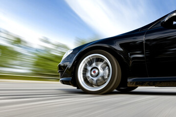 sleek black car speeds along road, its tire skidding on asphalt, creating dynamic motion blur effect against backdrop of blurred trees and sky