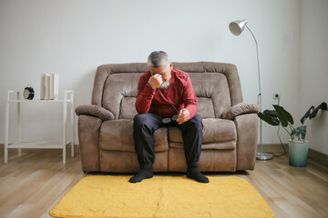Senior Man In Glasses Having Headache And Massaging Nose Bridge Sitting On Couch