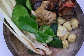 Various kinds of fresh herbs and spices are arranged on a wooden plate, consisting of lemongrass stalks, galangal, lime leaves, ginger, candlenuts. isolated on a white background.