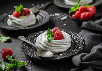 pavlova meringue dessert with raspberries and cream on a black background