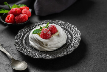 pavlova meringue dessert with raspberries and cream on a black background