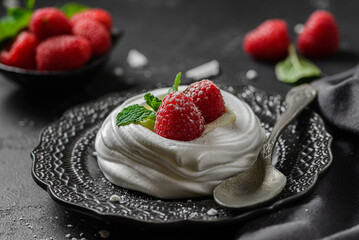 pavlova meringue dessert with raspberries and cream on a black background