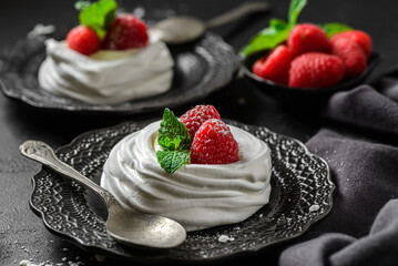 pavlova meringue dessert with raspberries and cream on a black background