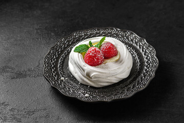 pavlova meringue dessert with raspberries and cream on a black background