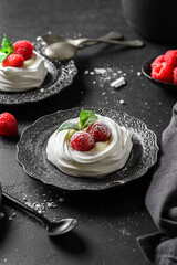 pavlova meringue dessert with raspberries and cream on a black background