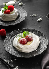 pavlova meringue dessert with raspberries and cream on a black background