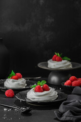pavlova meringue dessert with raspberries and cream on a black background