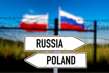 Polish and Russian flags behind barbed wire and sign with arrows pointing towards Russia and Poland