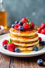 Delicious pancakes topped with fresh berries and syrup on a wooden table.