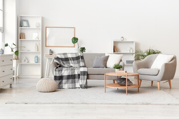 Interior of light living room with grey sofa, armchair and table