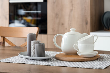 Grey candles and teapot with cups on table in kitchen, closeup