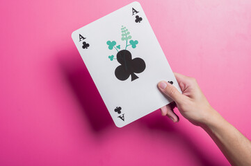 Asian hand holding oversized playing cards showing a royal flush in spades, set against a pink background. The composition suggests winning, gambling, strategy, or luck in a fun visual.