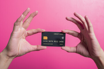 Close-up of an Asian hand holding a sleek black credit card with chip and contactless icon over a pink background, illustrating luxury, finance, and modern digital payment in studio lighting.