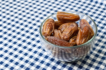 Close up view of kurma tunisia or sweet dried dates palm fruits in a little glass bowl isolated on napkin background. Copy space, empty space, free space.