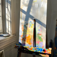 A sunlit canvas with abstract, colorful brushstrokes, positioned near a window.