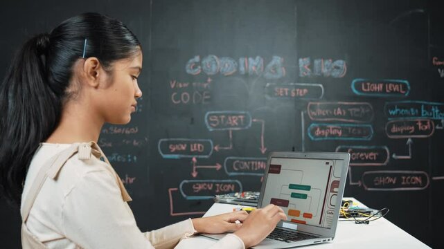 Caucasian girl working on laptop while smiling to camera at blackboard with engineering code and prompt written. Skilled pretty academic student learning programming or coding system. Edification