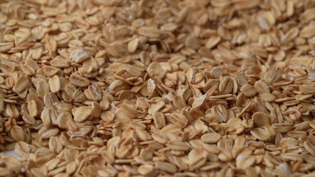 Slow motion, closeup footage of rolled oat flakes pouring over a pile of oats
