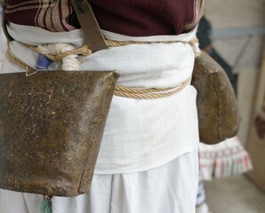 A close focus on large metal bells secured with rope and leather around a participant's waist, part of the Bulgarian Kukeri ritual used to chase away evil spirits and usher in good fortune