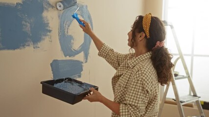 Woman painting wall indoors with roller tray ladder background in a bright room showcasing home improvement and diy skills in a new apartment environment.