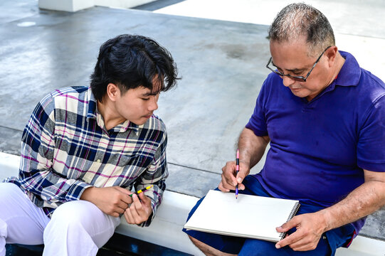 Asian male art student learning art with senior Caucasian teacher in outdoor workshop