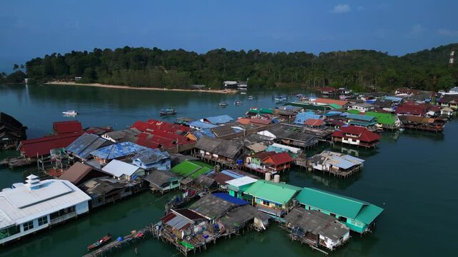 Bang Bao Pier floating village in Koh Chang island, Thailand, showing colorful houses and boats sailing in turquoise water. Dramatic aerial view flight overflight flyover drone