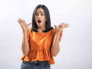 Obraz premium Surprised Southeast Asian woman with straight black hair wearing orange ruffled blouse and jeans, raising both hands beside face with cheerful expression against plain white background