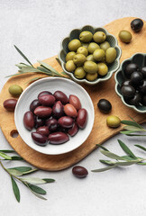 Kalamata, green and black olives displayed on wooden cutting board with olive branches