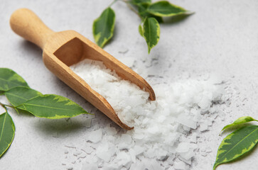 Magnesium flakes pouring from wooden scoop onto marble surface with green leaves
