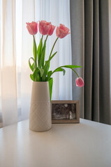 Pink tulips in vase and wedding photo on white table
