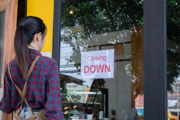 Asian businesswoman stands in front of café looking at a sign closing down, shutting down a small...
