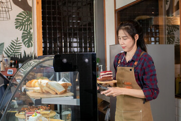 Beautiful Asian woman in apron bakery counts the number of cakes in a glass cabinet to check sales....