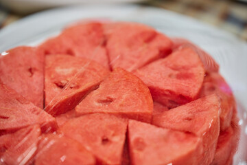 Close-up of chopped ripe watermelon on a plate wrapped with plastic bag