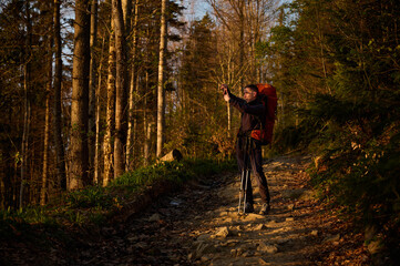 Fototapeta premium Fully equipped hiker taking pictures of sunrise on smartphone early in the morning in the mountains. Man standing with cell phone on mountain path enjoying sunrise.