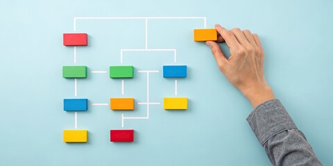 A hand manipulates colorful blocks on a flowchart against a blue background, illustrating organization or decision-making processes.