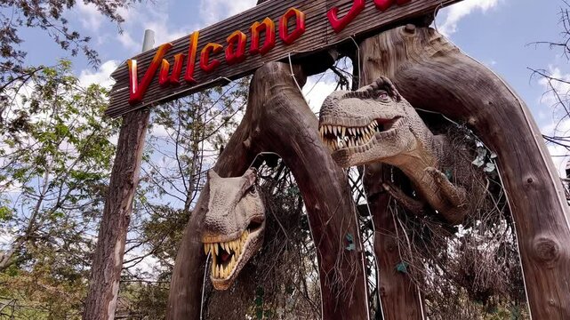 A sign above the entrance to an amusement park with dummies of prehistoric dinosaurs, the animals click their teeth, open their scary mouths