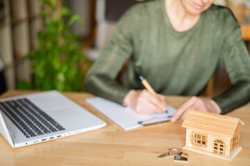 Real estate agent is signing a contract for a new home purchase, with a small wooden house and keys...