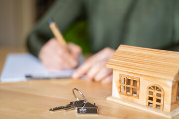 Real estate agent signing a contract for a new home purchase, surrounded by house keys and a small wooden model of a house on the office desk, symbolizing investment and future security