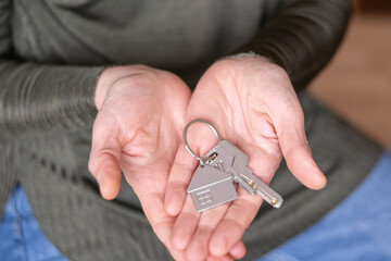 Real estate agent is holding house keys and a keychain in the shape of a house, symbolizing a new...