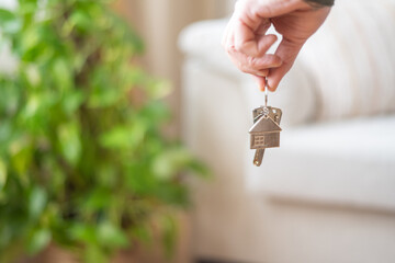 Real estate agent holding house keys with house shaped keychain in a blurred living room with a...