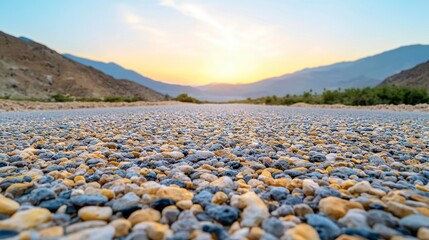 Gravel Road Leading to Sunlit Mountains at Sunset