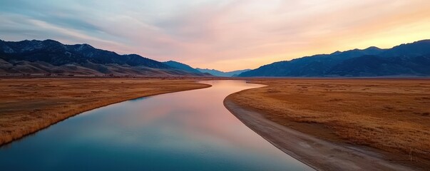 A serene river curves through a tranquil landscape, reflecting the soft hues of a sunset against mountains in the background.
