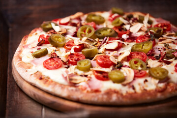 Pizza with ham, cherry tomatoes and mozzarella cheese. Wooden background. Soft focus. Close up.