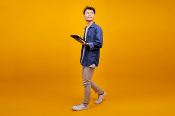 Full Body Of Cheerful Young Man Using Digital Tablet While Walking Over Yellow Background