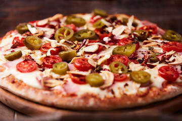 Pizza with ham, cherry tomatoes and mozzarella cheese. Wooden background. Soft focus. Close up.