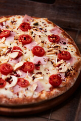 Pizza with ham, cherry tomatoes and mozzarella cheese. Wooden background. Soft focus. Close up.